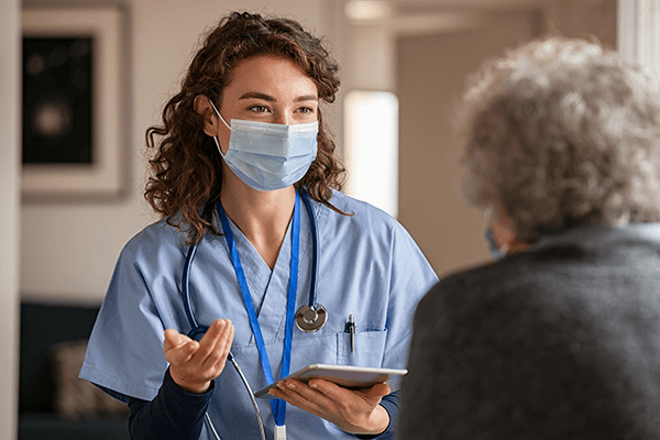 masked female health care worker talks to senior patient